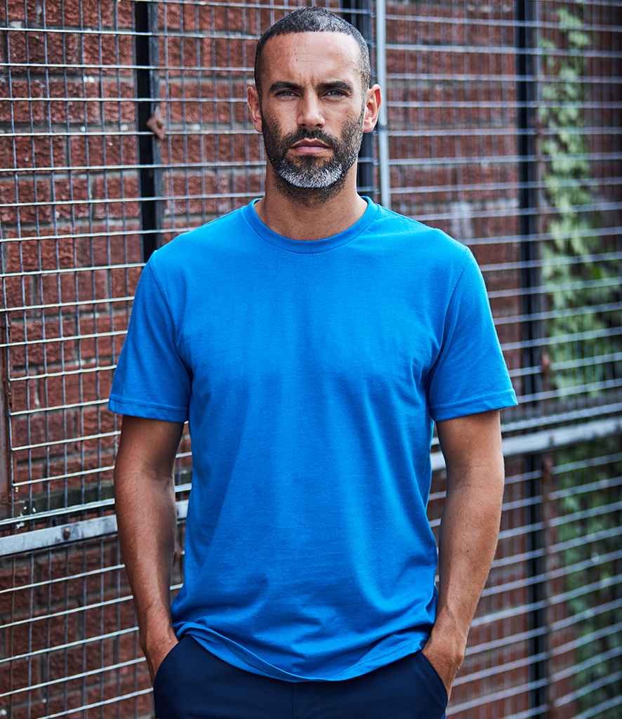 A man wearing a blue short-sleeved Pro T-shirt with a ribbed collar, standing in front of a fence.